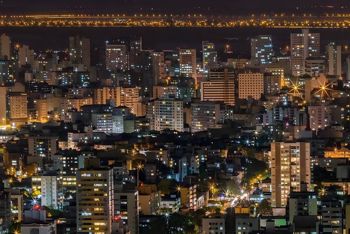 Nighttime aerial view of the Porto Alegre skyline featuring illuminated high-rise buildings and glowing street lights.