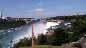 Panoramic view of the American Falls and Rainbow Bridge in Niagara Falls under a blue sky.