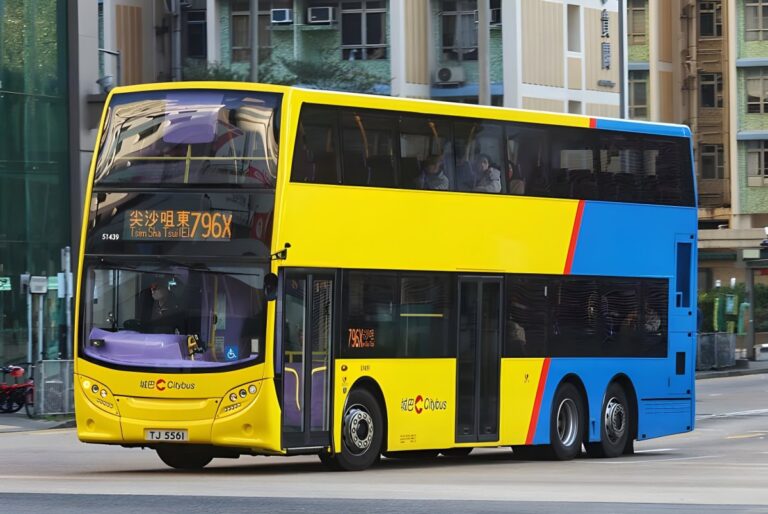 Yellow and blue Citybus double-decker bus driving on a Hong Kong city street in front of residential buildings.