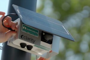 A person installs a solar-powered Clarity air quality sensor on a black utility pole.