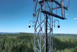 Two Pano AI 360-degree cameras mounted on a steel lattice tower overlooking a dense evergreen forest.