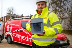 A Connexin engineer in high-visibility gear holds an IoT gateway in front of a branded red service van.