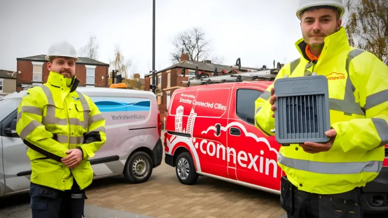 Two workers in high-visibility jackets stand by Yorkshire Water and Connexin vans, one holding a grey IoT gateway device.