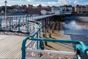 Penarth Pier with its wooden deck and teal railings extending over the water toward the coastal town buildings.