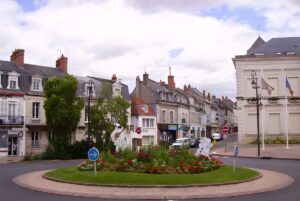 Street-level view of a landscaped traffic roundabout in Cosne-Cours-sur-Loire with traditional French architecture.