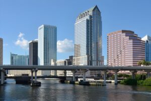Skyline of downtown Tampa, Florida, featuring high-rise office buildings and a concrete bridge over the Hillsborough River.