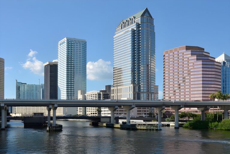 Skyline of downtown Tampa, Florida, featuring high-rise office buildings and a concrete bridge over the Hillsborough River.