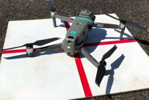 DJI Mavic quadcopter drone with a mounted sensor sitting on a white landing pad with red markings.
