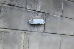 A Feelbat wireless monitoring sensor mounted over a vertical crack in a grey cinder block wall.