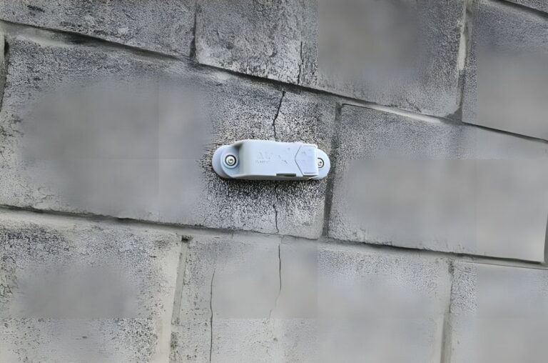 A Feelbat wireless monitoring sensor mounted over a vertical crack in a grey cinder block wall.