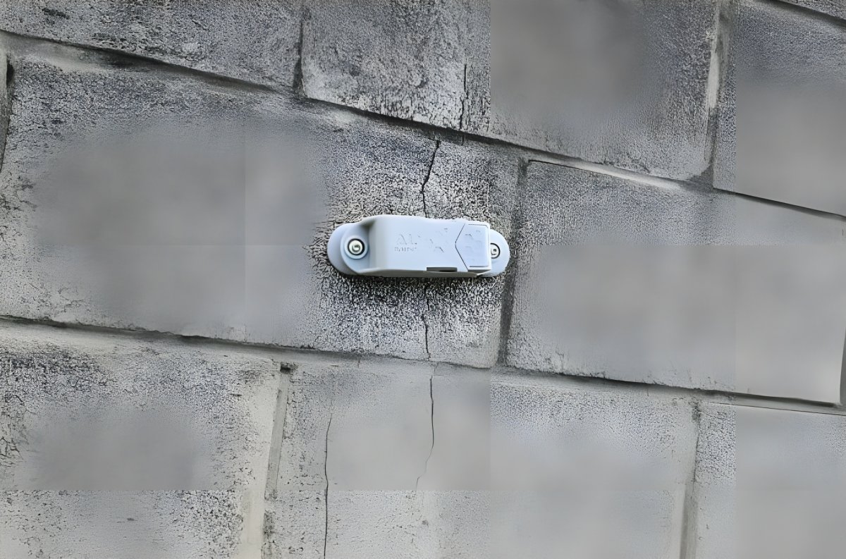 A Feelbat wireless monitoring sensor mounted over a vertical crack in a grey cinder block wall.