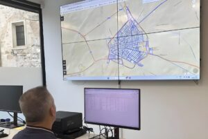 A technician views a digital hydraulic map of a city water network on a large wall-mounted monitor in a control room.
