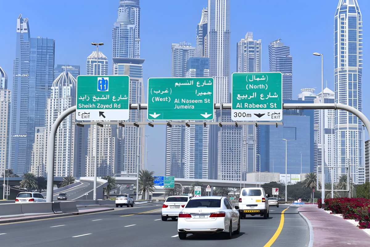 Green Dubai RTA road signs for Sheikh Zayed Road and Al Naseem Street over a multi-lane highway with city skyscrapers.