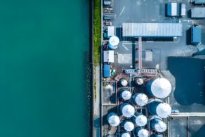 Aerial top-down view of an industrial water treatment facility with white storage tanks located next to a turquoise body of water.