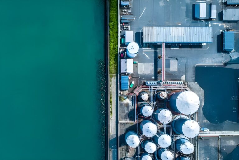 Aerial top-down view of an industrial water treatment facility with white storage tanks located next to a turquoise body of water.