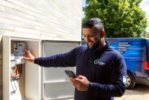 A Calisen technician uses a smartphone while inspecting a smart meter in an outdoor utility box next to a blue service van.