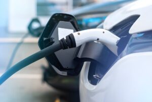 Close-up of a white electric vehicle plugged into a charging cable at a public station.