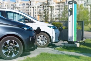 Two electric cars parked at a green and white curbside charging station in an urban residential area.