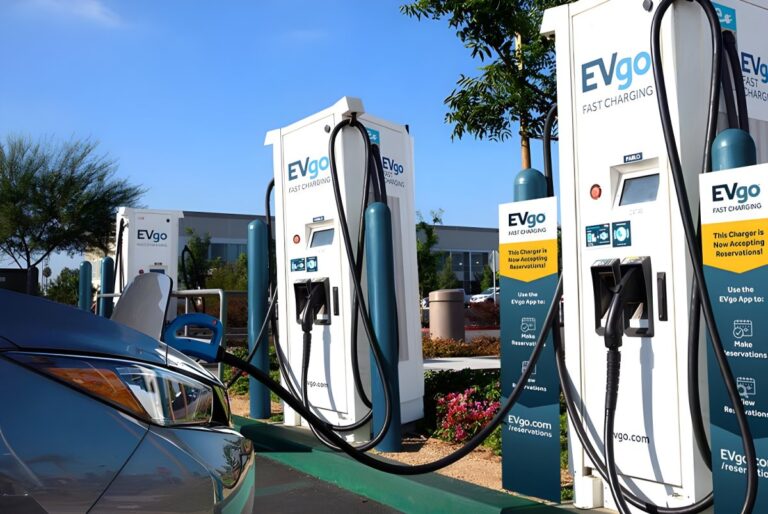 Row of EVgo fast-charging stations in a sunny outdoor parking lot with a car plugged into a charger in the foreground.
