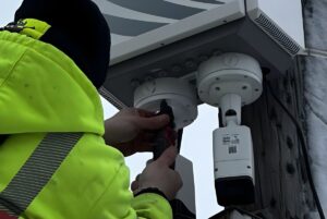 A technician in a high-visibility jacket installs Eagle Eye Networks security cameras onto a utility pole.