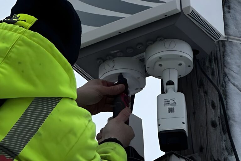 A technician in a high-visibility jacket installs Eagle Eye Networks security cameras onto a utility pole.