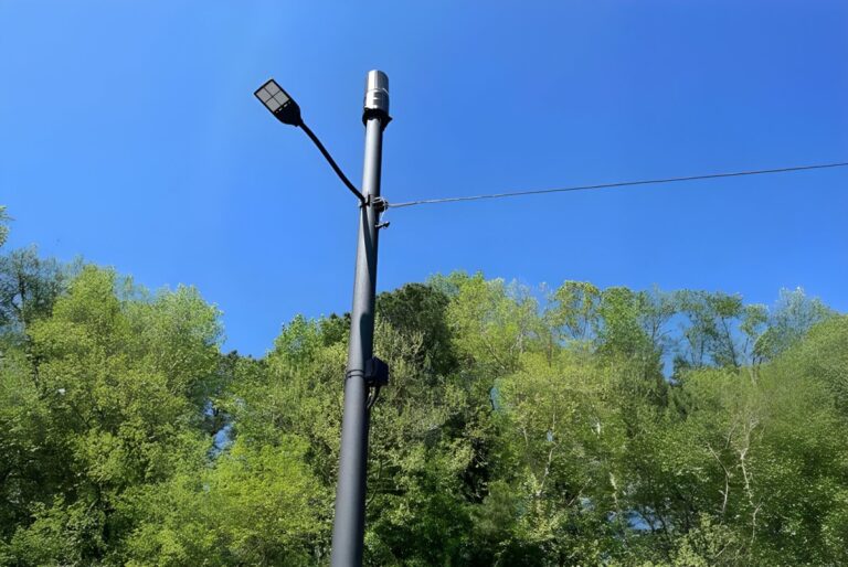 Black EasyStreet Systems smart pole with an integrated LED street light and wireless antenna against a clear blue sky.