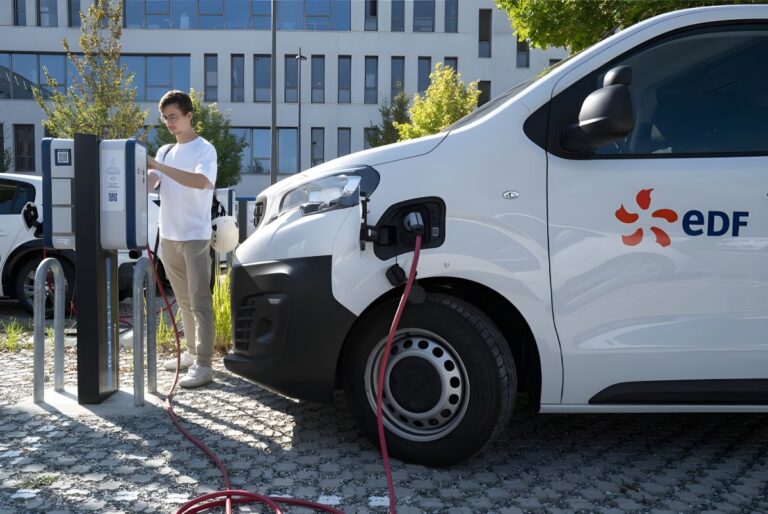 A man operates a vehicle-to-grid charging station connected to a white EDF branded electric van in an office parking lot.