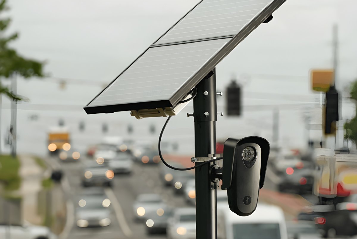 A Flock Safety license plate recognition camera and solar panel mounted on a pole overlooking a busy city road.