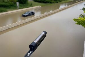 A Hyfi water level sensor mounted over a flooded highway with a partially submerged car.