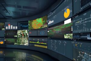 Curved wall of digital monitors displaying geospatial maps, electrical grid diagrams, and data analytics charts.