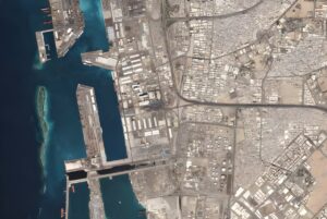 Satellite view of a coastal industrial port and dense urban grid with shipping terminals and highways.