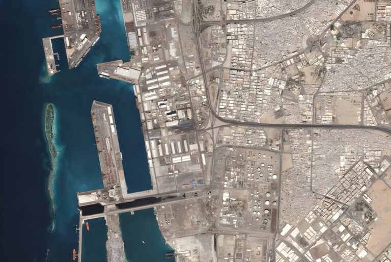 Satellite view of a coastal industrial port and dense urban grid with shipping terminals and highways.