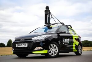 A Gaist branded mobile mapping vehicle with a roof-mounted 360-degree camera system parked on a rural road.