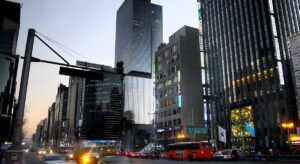 Traffic and buses moving through a dense Seoul city street lined with illuminated skyscrapers at dusk.