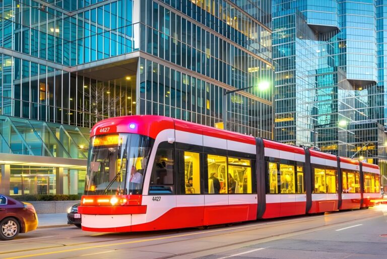 Red and white Toronto Transit Commission streetcar traveling past glass office buildings at dusk.