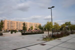 Modern street light pole in a paved urban plaza with trees and a multi-story residential building in Getafe Norte.