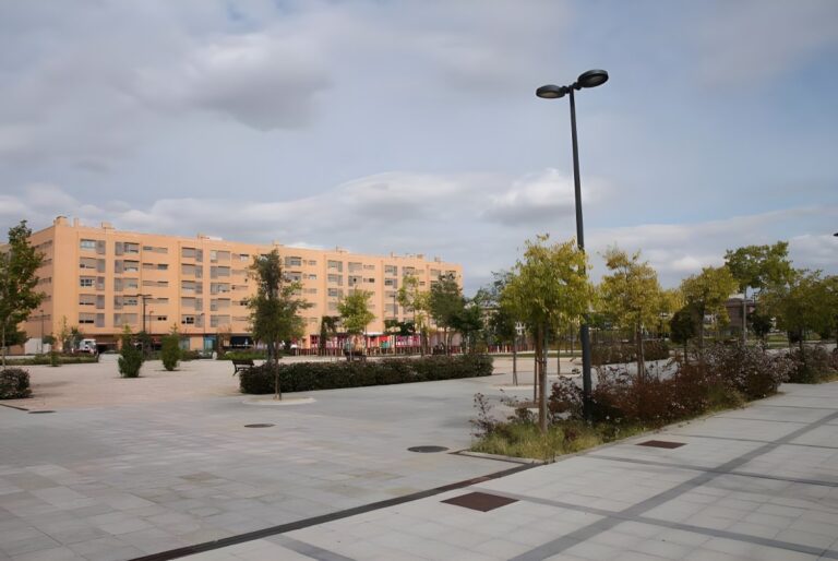Modern street light pole in a paved urban plaza with trees and a multi-story residential building in Getafe Norte.
