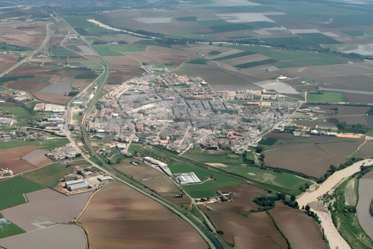 Aerial view of a small town in the Gran Vega region of Andalusia surrounded by agricultural fields and a winding river.