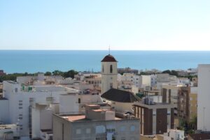 Elevated view of Guardamar del Segura rooftops and a church bell tower overlooking the Mediterranean Sea.