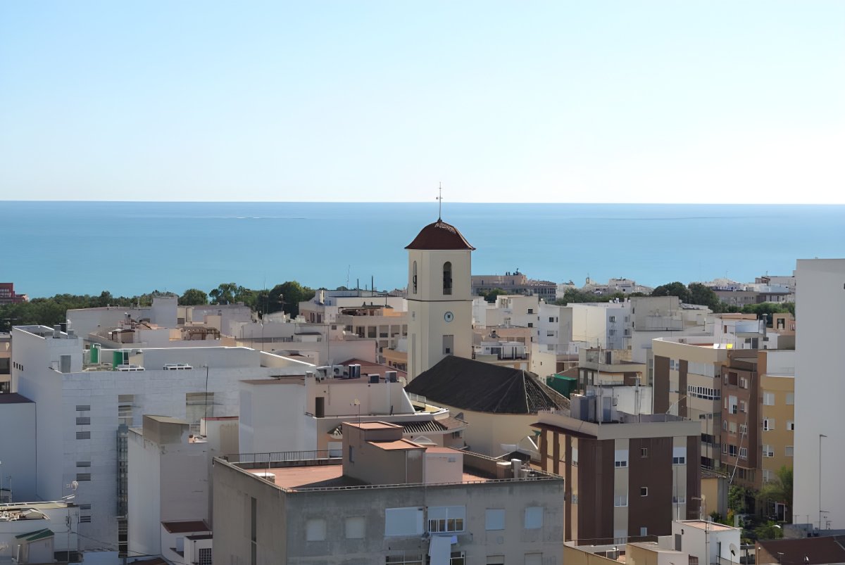 Elevated view of Guardamar del Segura rooftops and a church bell tower overlooking the Mediterranean Sea.
