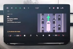 Vehicle infotainment screen displaying a digital safety alert for an approaching emergency vehicle in traffic.