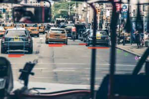 Hayden AI mobile sensor view from a bus dashboard identifying license plates and vehicles in a busy city street.