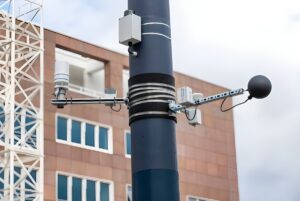 Environmental sensors and a black globe thermometer mounted on a blue utility pole in an urban setting.