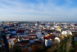 High-angle panoramic view of the Huelva city skyline featuring white buildings and red-tiled roofs under a blue sky.