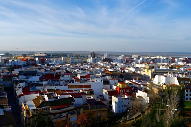 High-angle panoramic view of the Huelva city skyline featuring white buildings and red-tiled roofs under a blue sky.