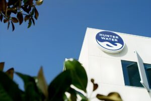 Low-angle view of the Hunter Water logo on a white building exterior under a clear blue sky.
