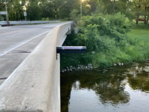 A Hyfi solar-powered flood sensor mounted to the concrete side of a bridge overlooking a river.
