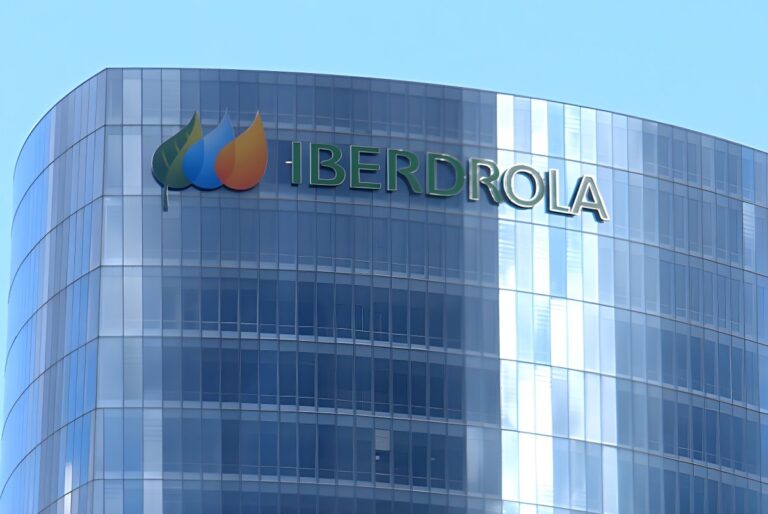 The Iberdrola logo and name mounted on the curved glass facade of a modern skyscraper against a clear blue sky.