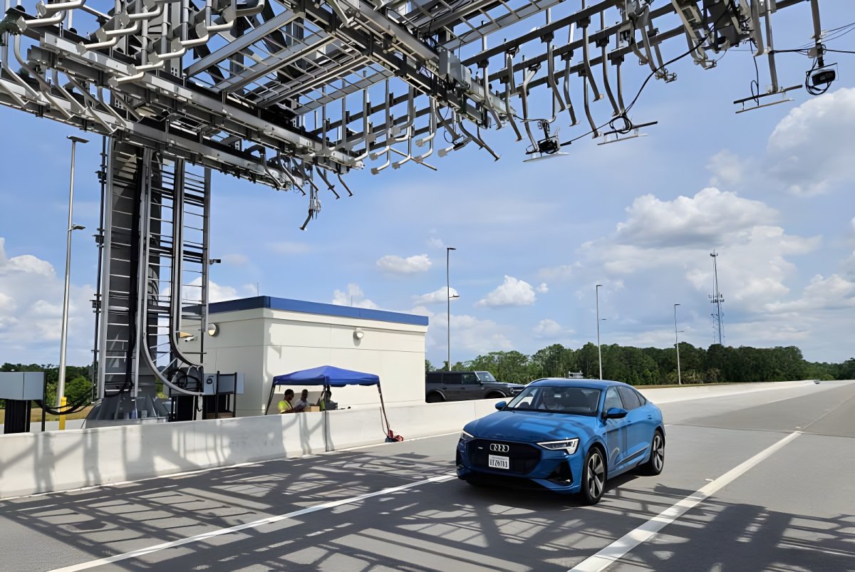 Blue Audi driving under an Indra overhead tolling gantry with sensors and cameras on a highway.
