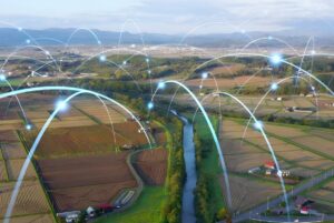 Aerial view of rural farmland and a river with digital blue light arcs representing a wireless network.